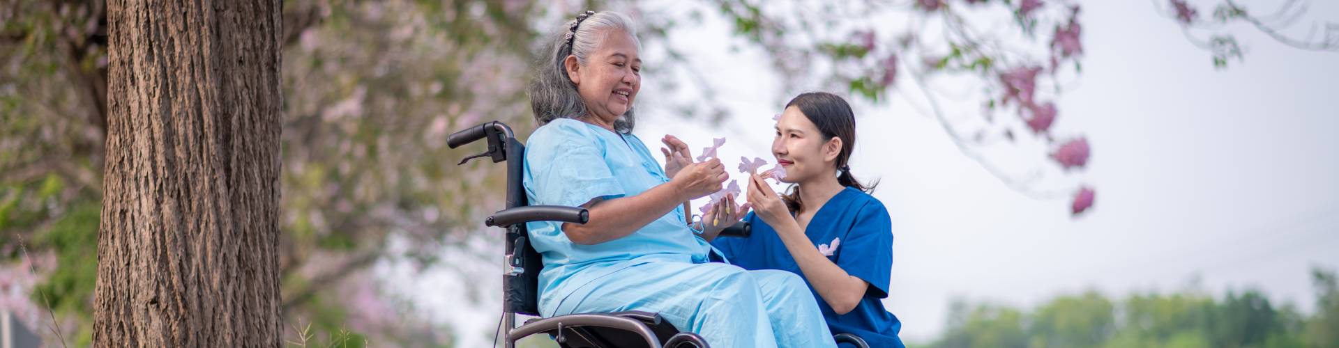 a caretaker and an elder woman in a flower field playing with flowers